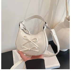 Close-up of cream glossy patent leather handbag featuring 3D bows and silver hardware