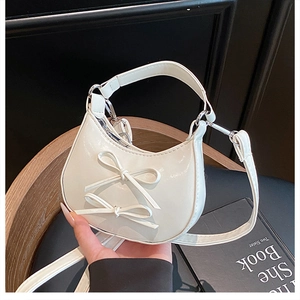 Detail of white glossy mini crescent bag with bows and silver hardware held in hand
