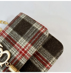 Detailed macro view of plaid tweed fabric with a gold heart pendant on a shoulder bag