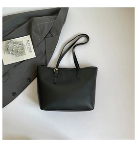 Detailed flat lay of a black leather tote bag with gold buckle and artistic props