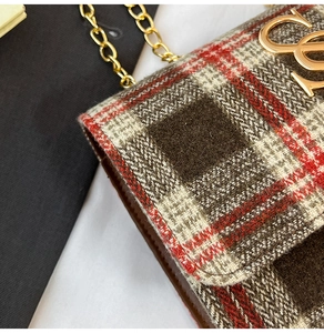 Detail of classic plaid fabric texture with gold metal interlocking logo on flap bag