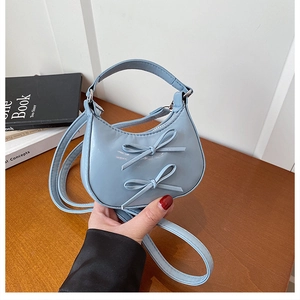 Close-up of light blue mini handbag with double bow accents and glossy leather texture