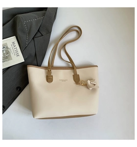 Platliggende beige draagtas met bruine riemen naast een blazer en kunstboek