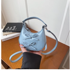 Detail of light blue glossy leather handbag with cute bow accents and adjustable strap
