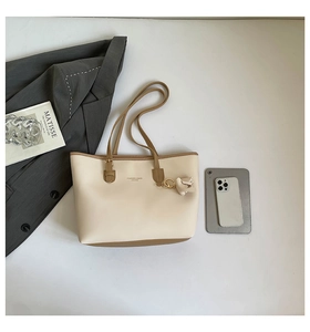 Detail of a minimalist cream tote bag with brown trim and floral charm for commuters