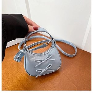 Detail of light blue mini handbag with sweet bows and silver hardware held by hand