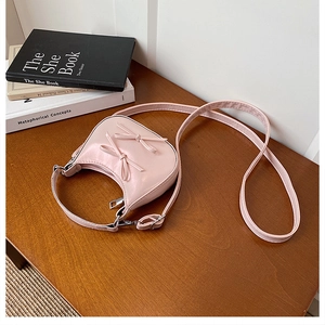 Detail of light pink semi-circle bag with 3D bows on a wooden table with books