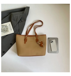Detail of khaki tote bag with dark brown handles and elegant bow pendant on white background