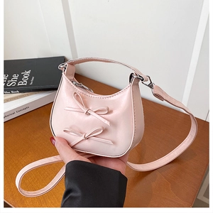 Close-up of pink crescent handbag featuring sweet bow details and top handle