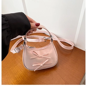 Detail of pink mini handbag featuring cute double bows and adjustable strap on a wood table