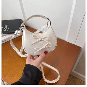 Close-up of cream mini crescent bag featuring dual bow accents and adjustable strap