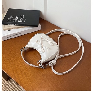 Detail of white glossy leather half-moon bag with decorative bows and silver hardware