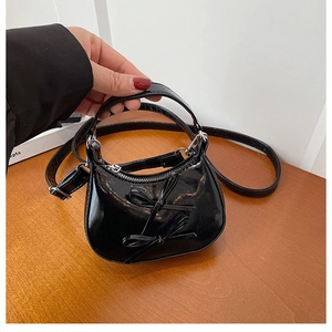 Detail of a black patent leather mini bag with a 3D bow and silver zipper on wooden table