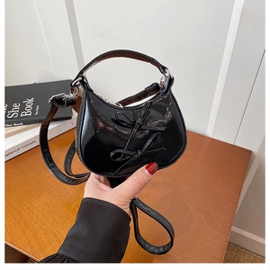 Detail of a black patent leather mini crescent handbag with cute double bow accents