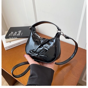 Close-up of black glossy patent leather handbag with decorative double bows detail