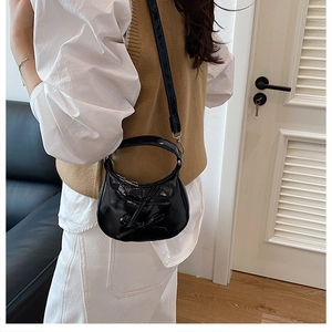 Detail view of black glossy half-moon shoulder bag featuring a decorative bow on the side