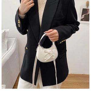 Mini white patent leather half-moon bag with bow details worn with a black blazer