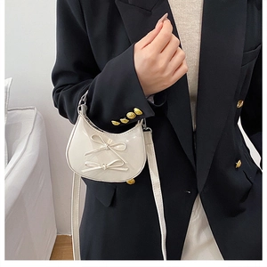 Detailed view of white half-moon crossbody bag with glossy finish and sweet bow accents