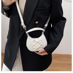 Mini white crescent handbag with bow details shown on model with black suit