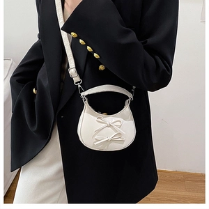 Detail of a creamy white mini crossbody bag featuring dual bows and glossy patent texture