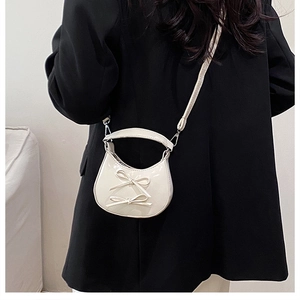 Detail of a creamy white crescent bag featuring cute bows and glossy leather finish