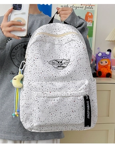 Detail of white backpack with black splash ink pattern, brand ribbon and moon pendant