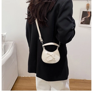 Detail view of a cream half-moon crossbody bag featuring decorative bows and a top handle