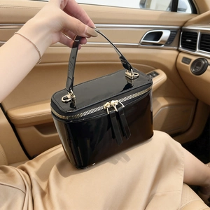 Glossy black patent leather box bag with gold zippers on luxury car seat background