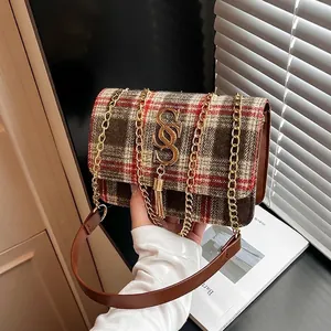 Chic plaid crossbody bag with gold metal logo and fringe tassel held in hand