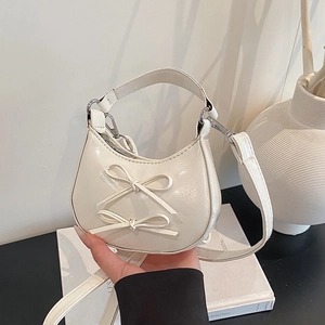Creamy white crescent handbag with bow details and glossy finish in a minimalist setting