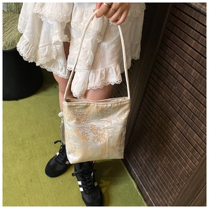 Detalle del bolso de hombro en satén crema con jacquard de paisaje dorado y asa fina