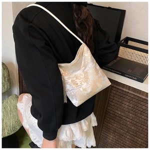 Detail of ivory satin jacquard bag with gold Chinese landscape pattern and tassel