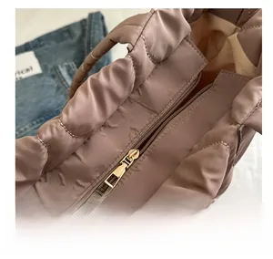 Close-up of smooth gold metal zipper on dusty pink quilted down tote bag