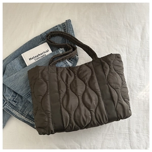 Detailed close-up of dark brown quilted puffer tote bag with wave stitching on white surface