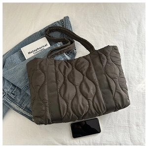 Macro detail of wave quilted texture on dark coffee puffer tote bag with phone for scale