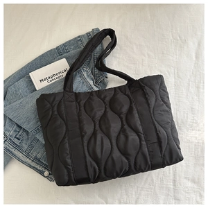 Flat lay of black quilted puffy tote bag with wavy stitching next to a denim jacket