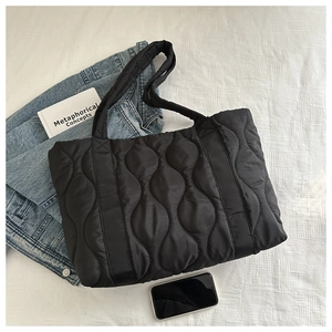 Top view of a black quilted puffer tote bag on a white fabric background with casual props