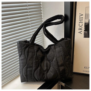 Detail of black quilted puffer tote bag featuring soft wave stitching and shoulder straps