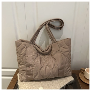 Detail of wave quilted puffer tote bag in dark khaki placed on a wooden table