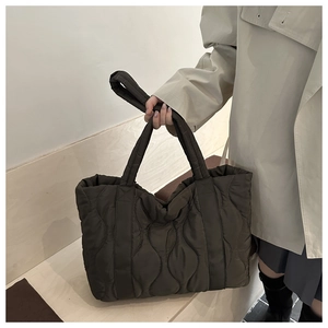 Detail of a large brown quilted puffer tote bag with elegant wave stitching and soft handle