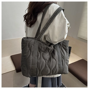 Detail view of large charcoal quilted tote bag with wavy stitching shown on shoulder