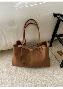 Detail of a brown tote bag featuring a gold buckle and slim straps in a minimalist setting