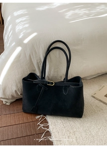 Close-up of black matte suede tote bag with gold buckle and slim straps on white carpet