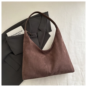 Detail of a brown suede hobo bag with a wide leather strap on a minimalist background