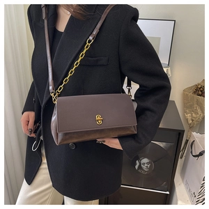 Detail of dark brown leather square bag with gold metal buckle on a black blazer model