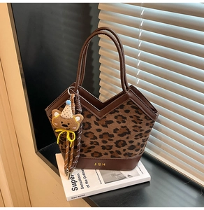 Detail of leopard print tote bag featuring a gold brand logo and cute bear charm