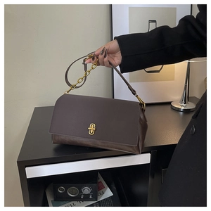 Detail of dark brown leather handbag featuring a golden oval twist lock and metal chain