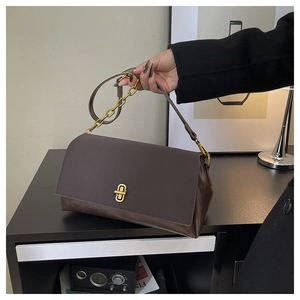 Detail of dark chocolate leather handbag with gold rectangular clasp and chain strap