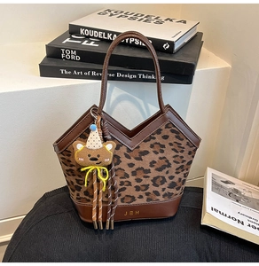 Detail of leopard print tote bag with dark brown leather handles and teddy bear charm