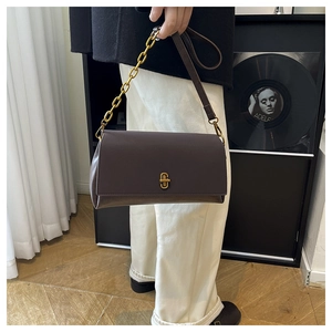 Detail view of deep brown square handbag featuring a gold buckle and metal chain strap